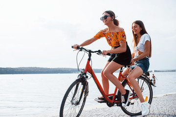 Obraz premium Two female friends on the bike have fun at beach near the lake