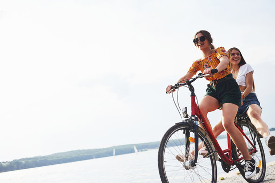 Two female friends on the bike have fun at beach near the lake © standret