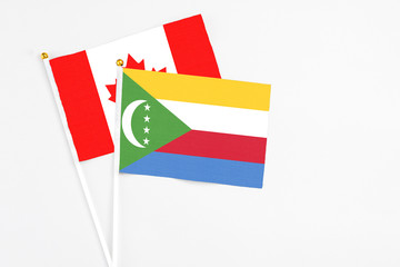 Comoros and Canada stick flags on white background. High quality fabric, miniature national flag. Peaceful global concept.White floor for copy space.