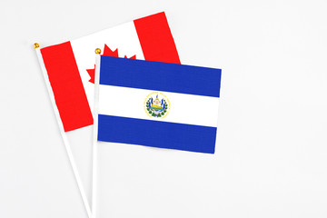 El Salvador and Canada stick flags on white background. High quality fabric, miniature national flag. Peaceful global concept.White floor for copy space.