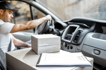 Delivery man driving cargo vehicle with parcels on the passenger seat, image focused on the cardboard boxes with blank space