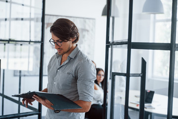 Man in glasses with notepad and pen in hands stands in the office opposite employees