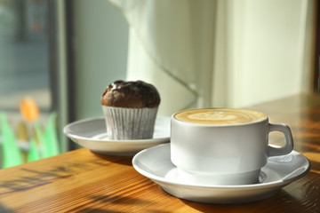Cup of fresh aromatic coffee and cupcake at table in cafe