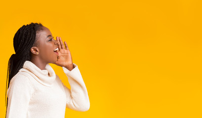 African american winter woman screaming with excitement over yellow background