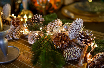 Obraz na płótnie Canvas Christmas decorations on a large wooden table. Fir cones and branches are sprinkled with snow and decorated with a garland.