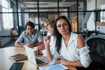 Brunette woman in front of employees. Young business people in formal clothes working in the office