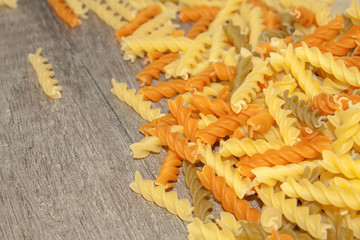 Scattered multicolored pasta spirals on a wooden background. View from above. Copy space.