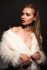 sexy naked young woman in white faux fur coat isolated on black