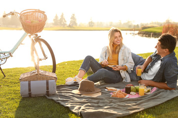 Happy young couple having picnic near lake on sunny day