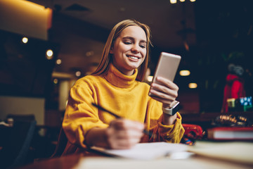 Pretty prosperous blonde woman dressed in cool yellow sweater using smartphone application for...