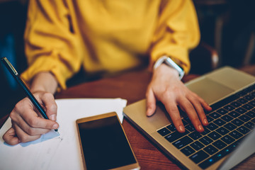 Cropped image of female hands with pen writing notes for course work using laptop computer, young...
