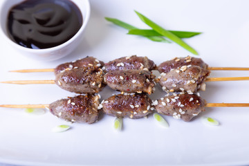 Grilled chicken hearts on wooden skewers with sesame seeds and teriyaki sauce. Selective focus, close-up.