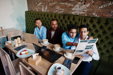 Group of four south asian men's posed at business meeting in cafe. Indians work with laptops together using various gadgets, having conversation and look at the menu.