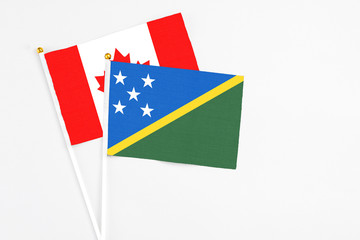 Solomon Islands and Canada stick flags on white background. High quality fabric, miniature national flag. Peaceful global concept.White floor for copy space.