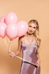 elegant blonde woman in violet satin dress and necklace holding pink balloons on beige