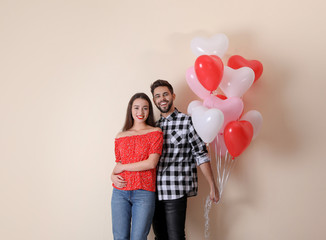 Beautiful couple with heart shaped balloons on beige background. Valentine's day celebration