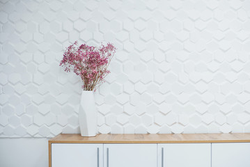 Simple interior of room with white textured walls and flowers on the table