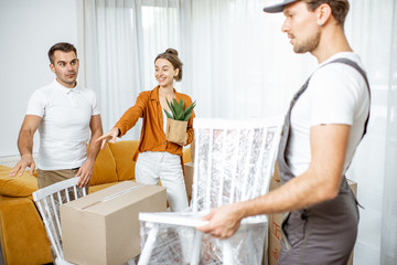 Obraz premium Young couple in the living room of their new home, mover performs professional furniture delivery during the relocation