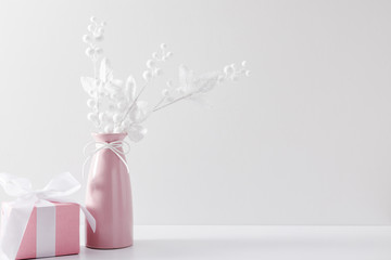 Winter composition of white branches, berries and leaves with sparkles in pink vase, gift on white background. Christmas, New Year, winter concept. Front view, copy space