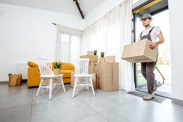 Handsome mover in workwear performing professional delivery of a goods and furniture during relocation process to a new house, interior view