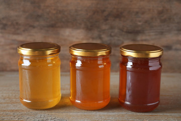 Jars with different types of organic honey on wooden table