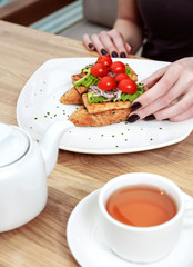 Female hands holding vegan sandwich with grilled tofu, avocado, cherry tomato, vegetables and scrambled tofu. Chef cooking. Vegan open sandwiche. Healthy food concept.