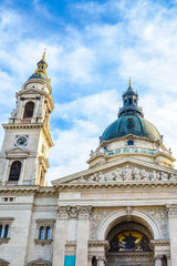 Fototapeta na wymiar Vertical picture of the front side facade of Saint Stephen's Basilica in Budapest, Hungary with blue sky and clouds above. Roman Catholic basilica built in neoclassical style. Left tower and cupola