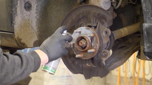 Mechanic spraying lubricant on a rusty wheel stud before replacing the brake system