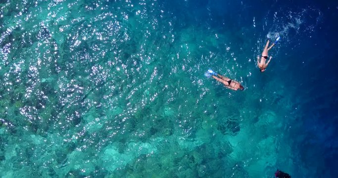 Young people snorkel and swim on clear emerald sea water watching beautiful corals and fish in Bora bora