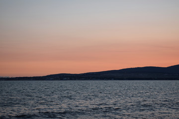 Naklejka premium Sunset over the sea. The Sun sets behind the mountains