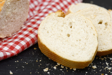 rustic crusty white bread lying on black slate on red white towel in the kitchen