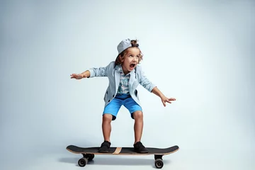 Fotobehang Skateboard Pretty young boy on skateboard in casual clothes on white studio background. Riding and looks happy. Caucasian male preschooler with bright facial emotions. Childhood, expression, having fun.  © master1305