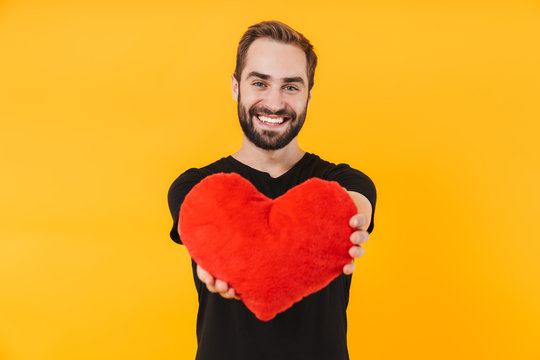 Image of lovely man wearing t-shirt smiling and holding red paper heart