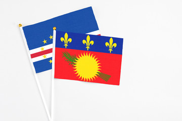 Naklejka premium Guadeloupe and Cape Verde stick flags on white background. High quality fabric, miniature national flag. Peaceful global concept.White floor for copy space.