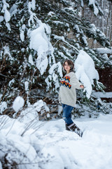 Fototapeta na wymiar A smiling girl of Caucasian appearance in a sweater and jeans on a background of snowy trees. Snowy winter day. A fun walk.