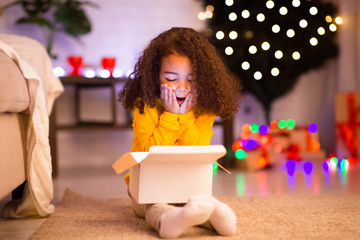 Amazed little afro girl opening Christmas gift near xmas tree
