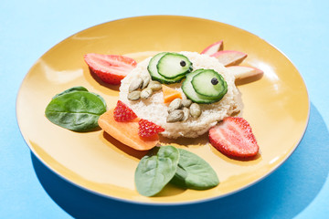 close up view of plate with fancy face made of food for childrens breakfast on blue background