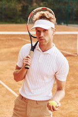 Holds ball in hand. Young tennis player in sportive clothes is on the court outdoors