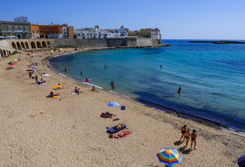 Sunbathing people on the beach of the mediterranean harbor at the travel destination Gallipoli in Puglia
