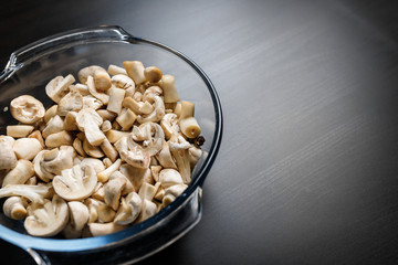 Cut forest champignon mushrooms in glass bowl on dark background or black wooden table.