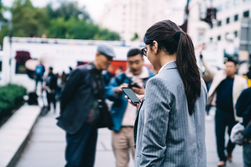 Back view of intelligent female employee reading received email on smartphone gadget connecting to public internet during work break in financial district, professional expert checking money balance