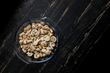 Cut forest champignons in glass bowl on black boards. Mushrooms on dark background.