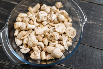 Cut forest champignons in glass bowl on black boards. Mushrooms on dark background.