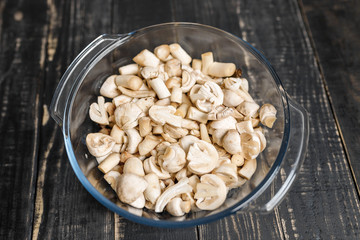 Cut forest champignons in glass bowl on black boards. Mushrooms on dark background.