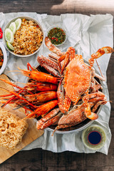 Top view of Steamed Giant Mud Crabs, Grilled Prawns (Shrimps), Crab Fried RIce, Pepper and Garlic Soft-Shell Crab, Crispy Catfish, Mango Salad and Thai spicy seafood sauce.