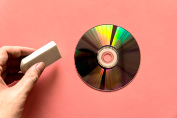 Hand pinching rubber over light reflected compact discs (CD) or digital versatile disc (DVD) on the pink paper background. Erasing data.