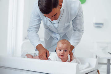 Fototapeta premium Young pediatrician is with little baby in the clinic at daytime