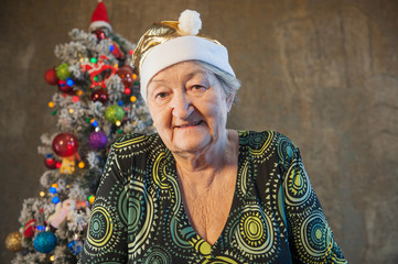 Fototapeta premium Extravagant old woman with gray hair and wrinkles in glasses. Senior citizen in santa claus hat. Concept of domineering and funny elderly mother in law. Christmas Eve