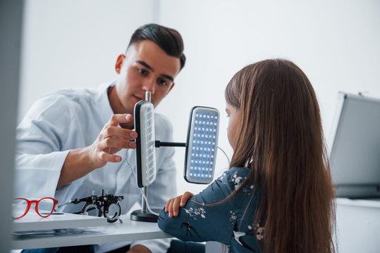 Two panels on the table. Young ophthalmologist is with little female visitor in the clinic