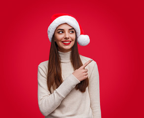 Cheerful young woman in Christmas hat pointing over shoulder